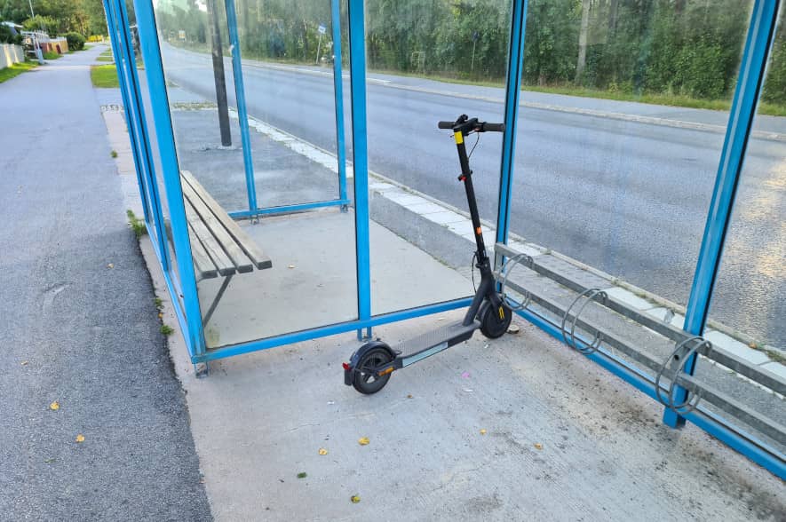 elsparkcykel vid busshållplats, parkerad i cykelställ